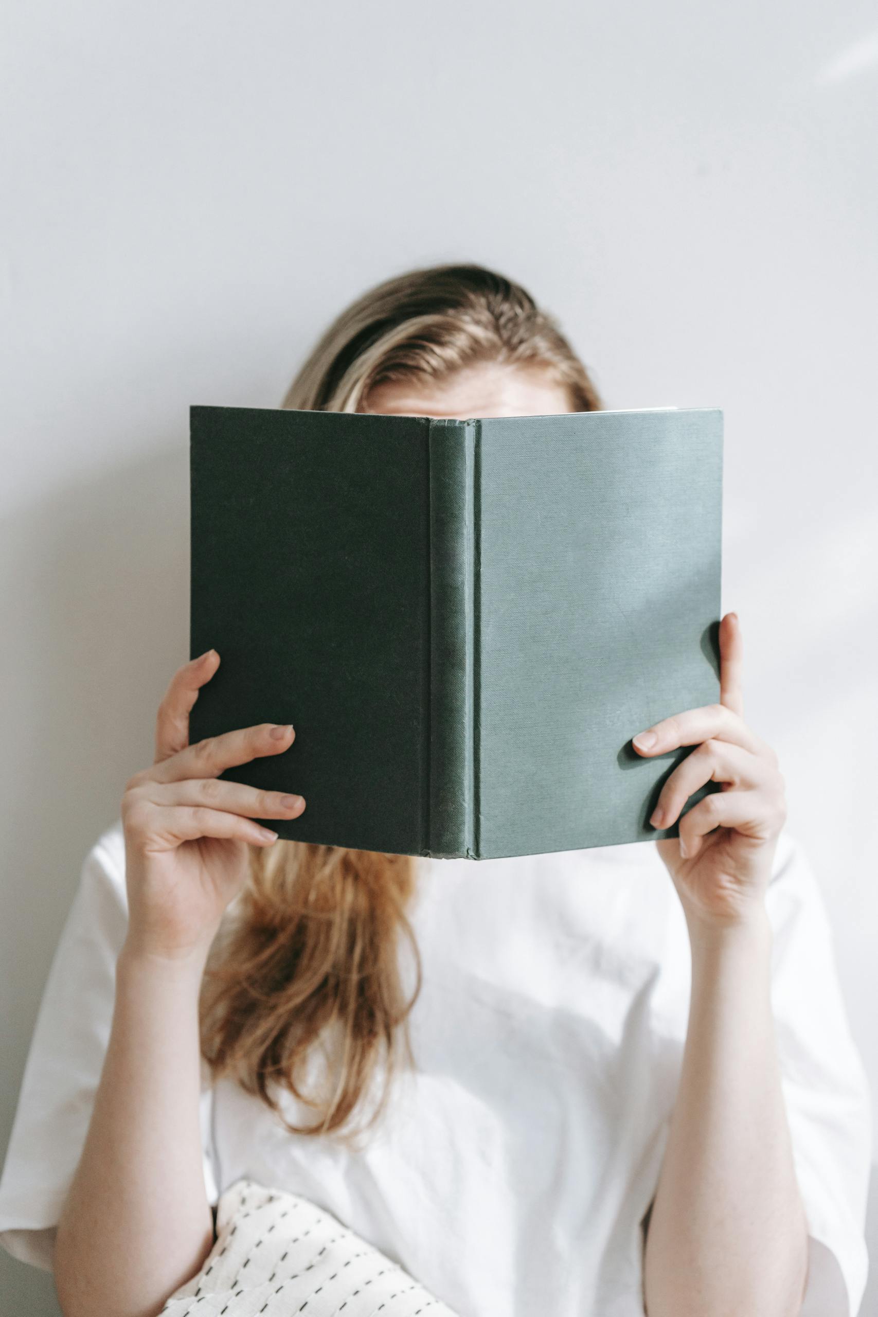 Unrecognizable student behind book studying in sunlight